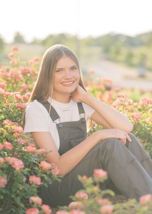 A person in casual attire poses among pink flowering bushes in warm natural lighting.
