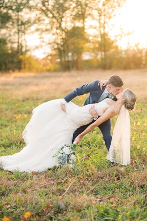 A romantic couple poses in golden sunlight on grassy terrain during sunset.