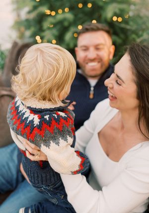 A family shares a joyful moment together in front of a Christmas tree with twinkling lights in the background.