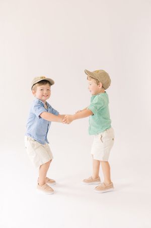 Two toddlers in casual summer outfits playing and interacting with each other against a white background.