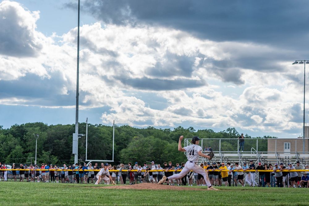 Wide-angle shot of Conwell-Egan Catholic High School pitcher Brady Guzzie in the wind-up. A crowd stands along the first base side.