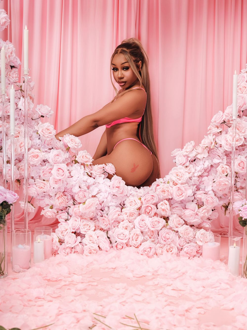 A pink-toned photoshoot setup with white floral decorations and draped fabric creating a romantic backdrop.