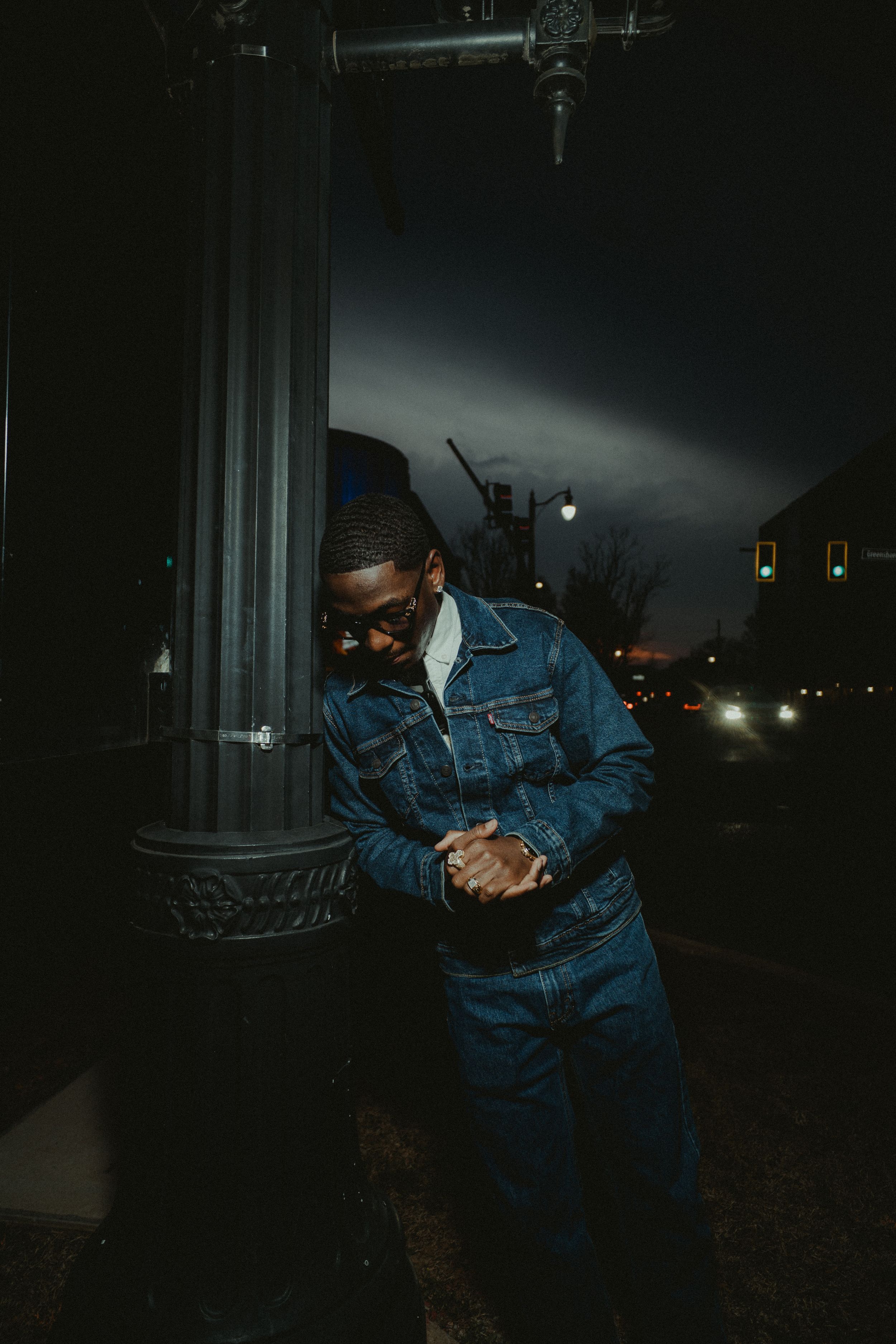 A person in denim clothing crouches in the darkness while holding what appears to be a flashlight.