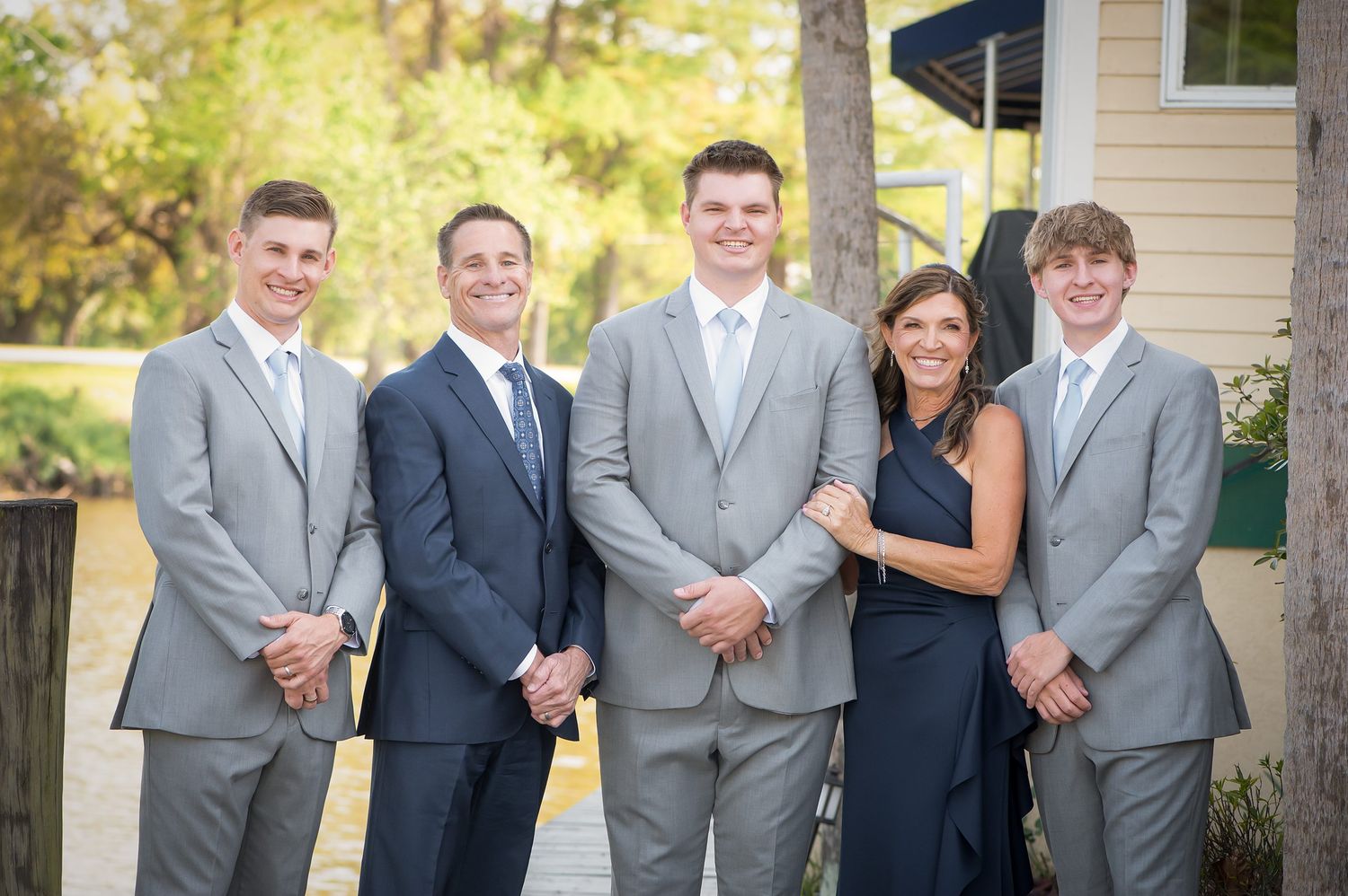 Family of five posing outdoors in formal attire, men in gray and navy suits, woman in navy dress.
