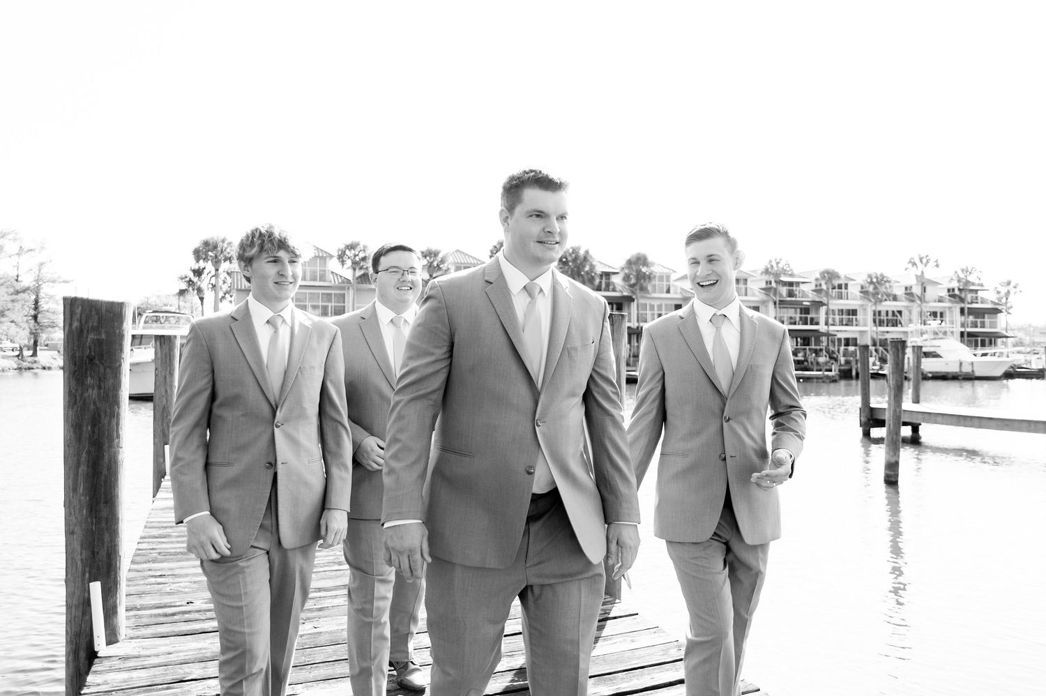 Groom and groomsmen in gray suits posing on a waterfront dock in a black and white wedding photo.