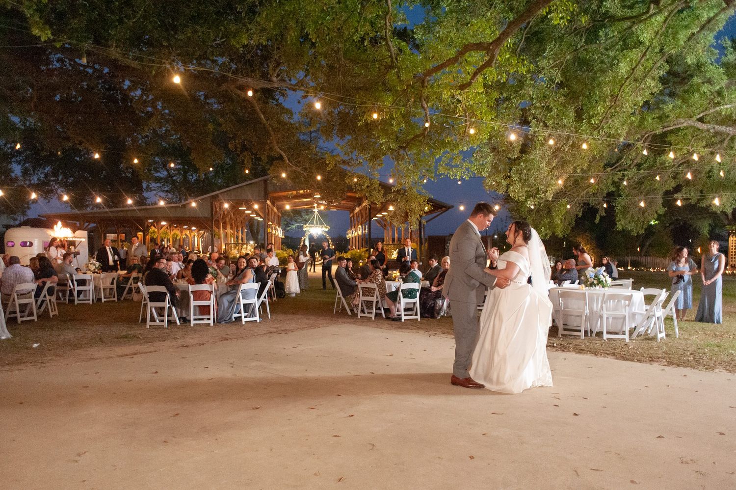 Couple shares first dance under canopy of string lights at romantic outdoor wedding reception at night.