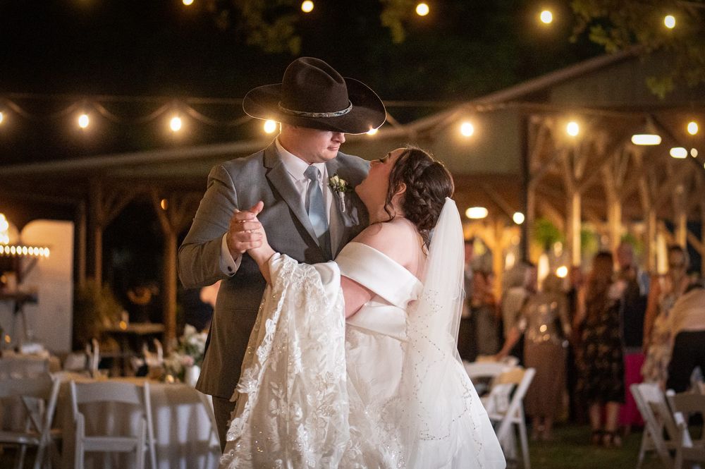 Bride and groom share first dance outdoors at night under string lights at rustic country wedding reception.