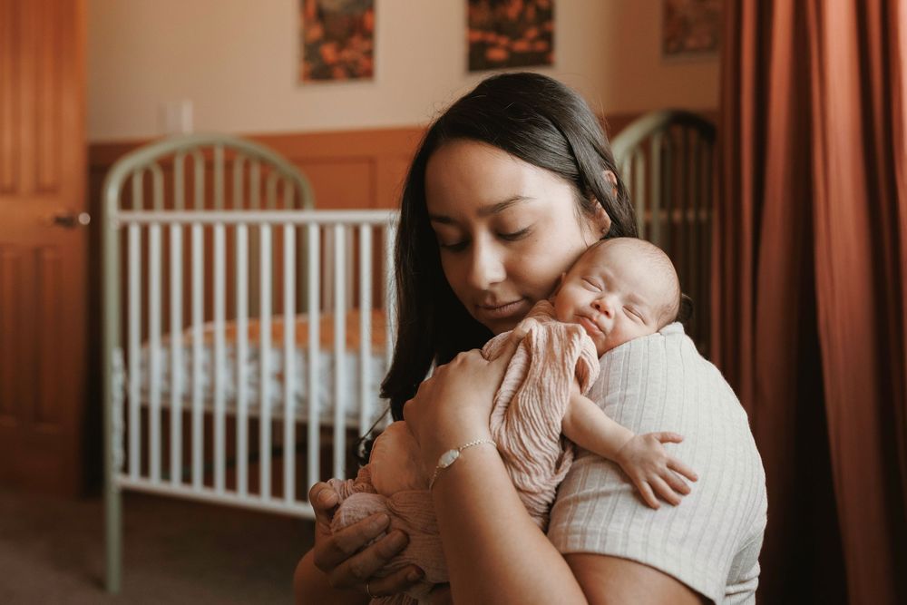 Mother gently kissing her sleeping newborn baby held in her arms in a warm nursery.