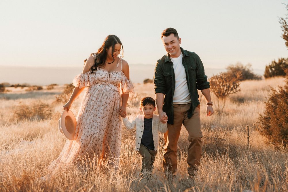Happy family with young boy walking through golden field at sunset.