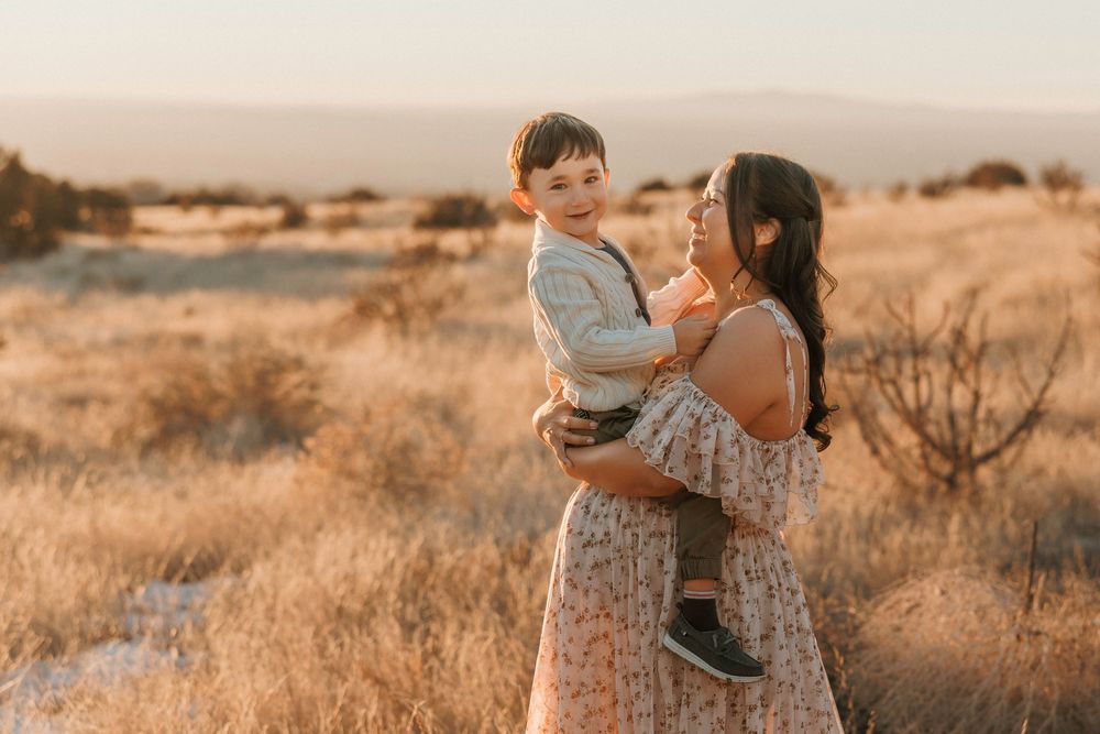 A mother lovingly holds her young son in a sunlit golden field at sunset.