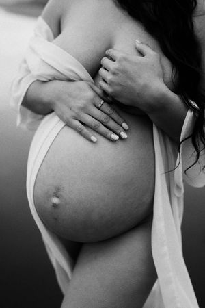 Black and white intimate maternity photo showing hands tenderly placed on a pregnant belly with a wedding ring visible.