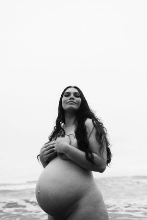A monochromatic artistic portrait of an expectant mother by the ocean at sunset showcasing her maternity silhouette.