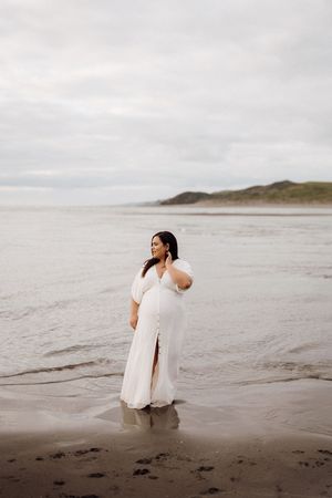 Two people in white outfits walking along a misty beach at sunset with coastal sand dunes in the background.