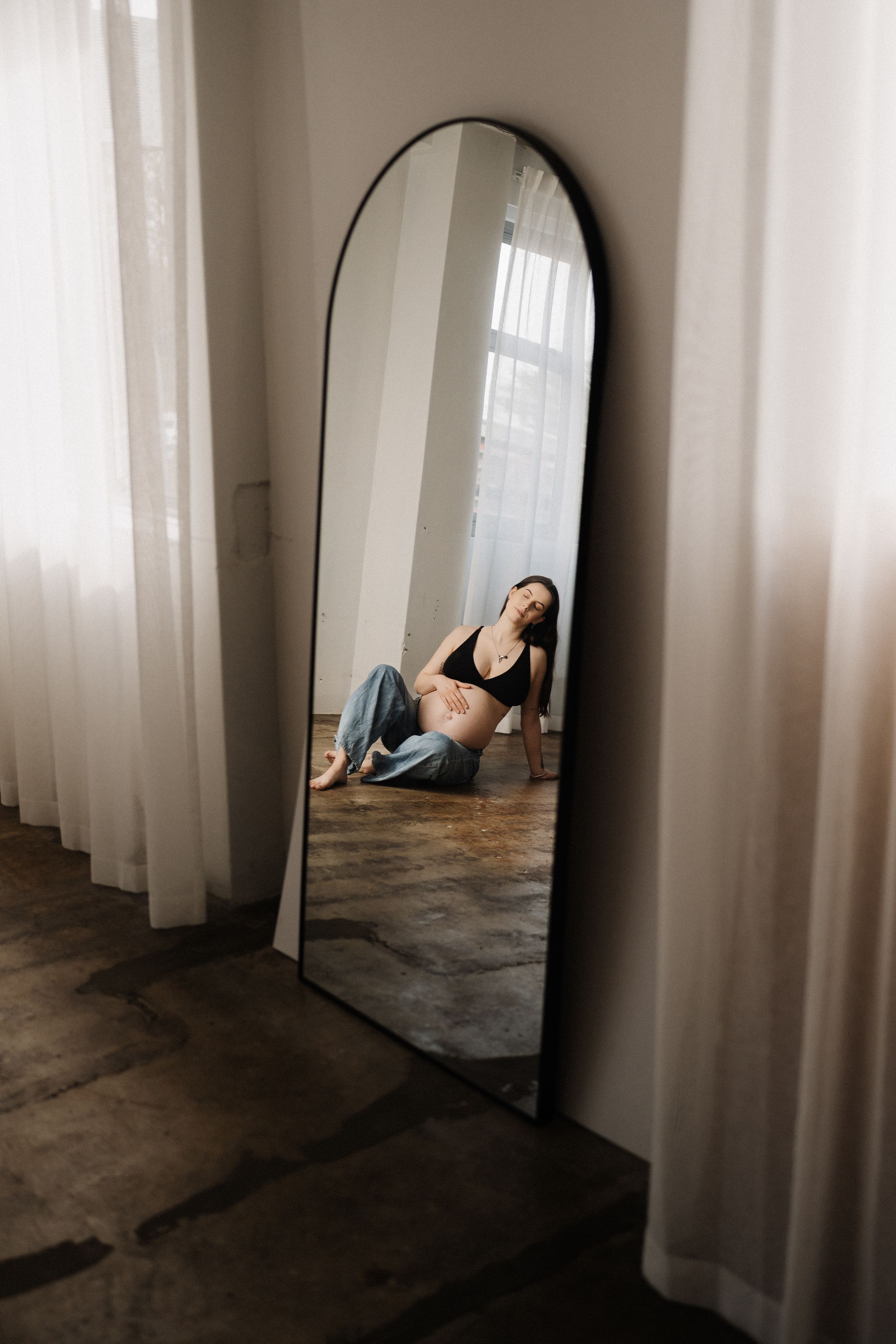 A series of mirrored reflections show a person lying on a concrete floor beside sheer white curtains in a minimalist space.