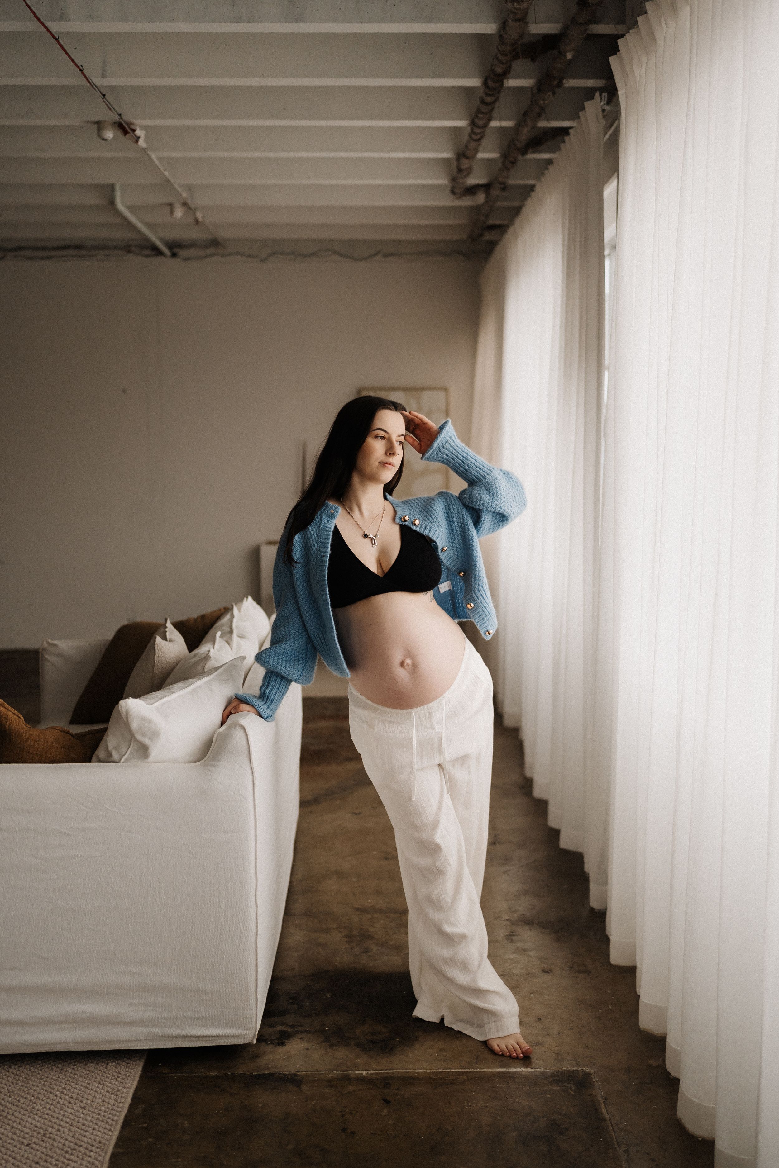A maternity photoshoot showing a flowing movement sequence in white pants and blue sweater against a minimalist interior.