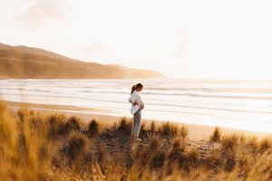 Two people stroll on a sandy beach at sunset with coastal hills in the background.