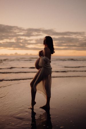 Silhouette of a couple sharing an intimate moment on a misty beach at sunset, casting reflections in the wet sand.