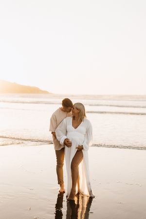 Romantic couple embracing on beach during golden hour sunset.