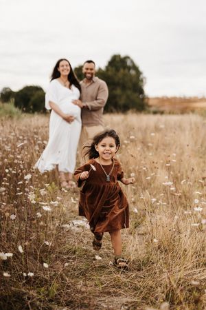 Young child in brown dress running joyfully through wildflower field.