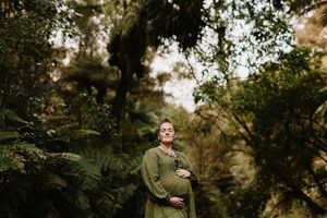Maternity portrait in green dress amid lush forest setting.