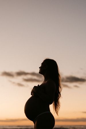 Silhouette of pregnant woman's profile against sunset sky showing her baby bump.