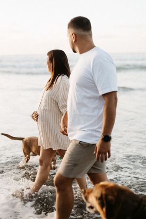 Couple plays with their dog in the shallow ocean waves at sunset.