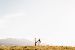 Two figures stand in silhouette on a hilltop during golden hour with mountains in the distance.