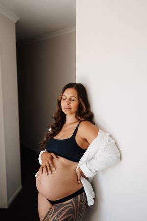 A series of minimalist maternity photos showing a pregnant woman in black against white walls in different poses.