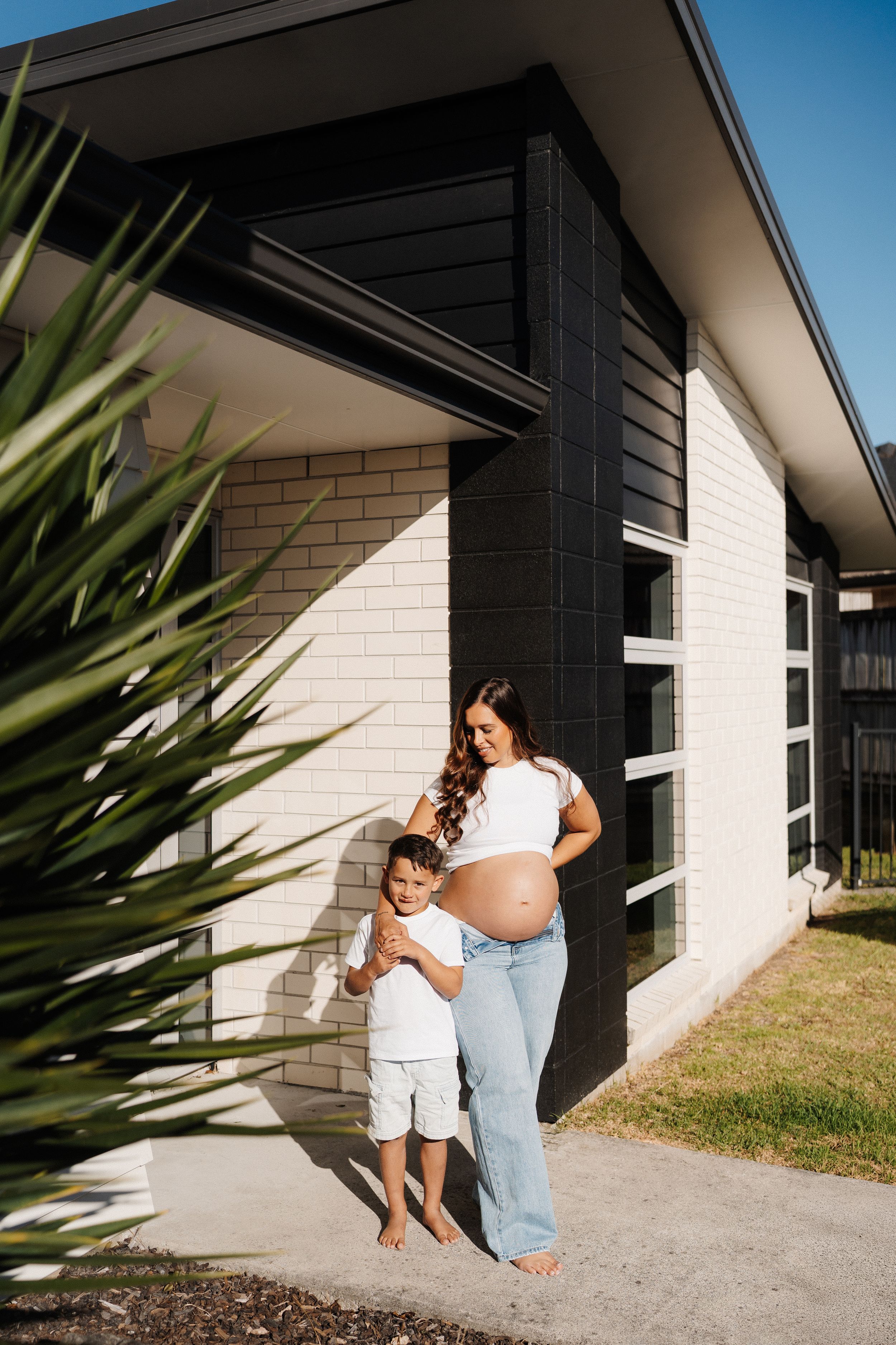 Series of outdoor photos showing a pregnant woman and small child by a modern white house with black trim.
