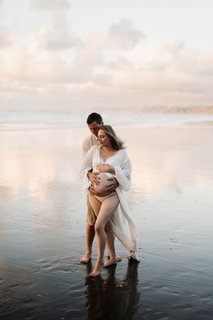 Couple shares intimate moment on reflective beach during sunset.