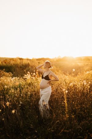 Figure in flowing white dress dances through tall grass field at sunset.
