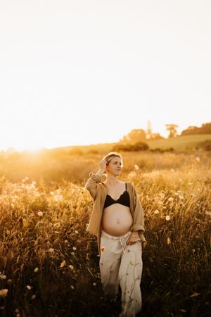 Person in white top poses gracefully in a golden wildflower field at dusk.