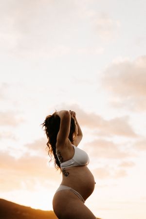 Silhouette of pregnant woman in white bikini against raglan sunset sky.