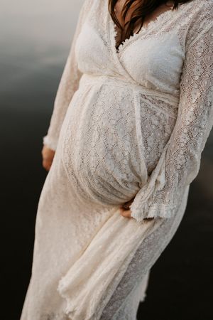 Close up of a white lace maternity dress showing details of the fabric and pregnant belly.