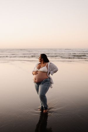 Expectant person standing barefoot in wet sand at beach during golden hour.