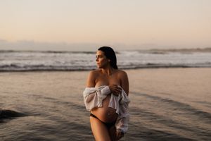 Silhouetted figure poses on beach in flowy white top during golden sunset.