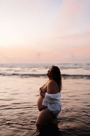 Silhouette of person standing in ocean water during pink sunset.