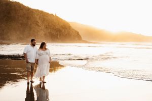 Couple walking along misty beach shore during golden sunset.