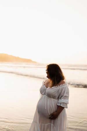 Person in white dress standing on beach during golden sunset hour.