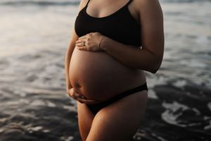 Side view of expectant mother cradling baby bump on beach at golden hour.
