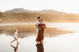 Family enjoying sunset together on reflective beach with mountains in background.
