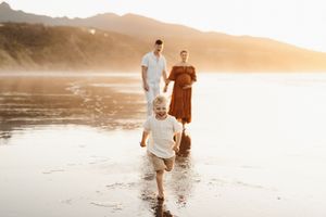 Family playing together on wet sandy beach during golden sunset hour.