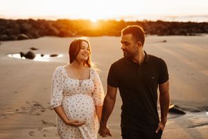 Expectant couple sharing intimate moment on beach during Raglan golden hour.
