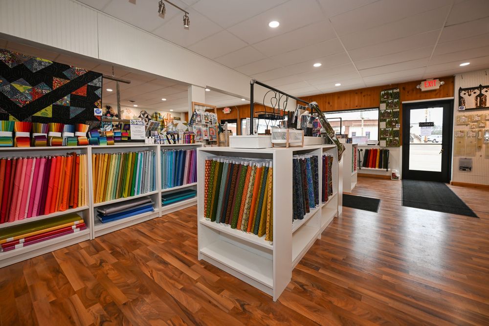 Colorful fabric bolts displayed on white shelving units in a bright, well-organized quilt and fabric retail store.