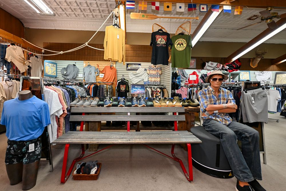 Man sitting on bench inside a casual clothing retail store with apparel displays and nautical flag decorations.