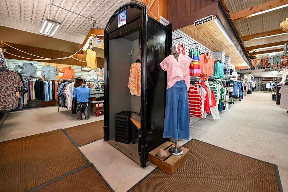 Retail clothing store interior with mannequin displaying pink top and blue skirt near a black fitting room.