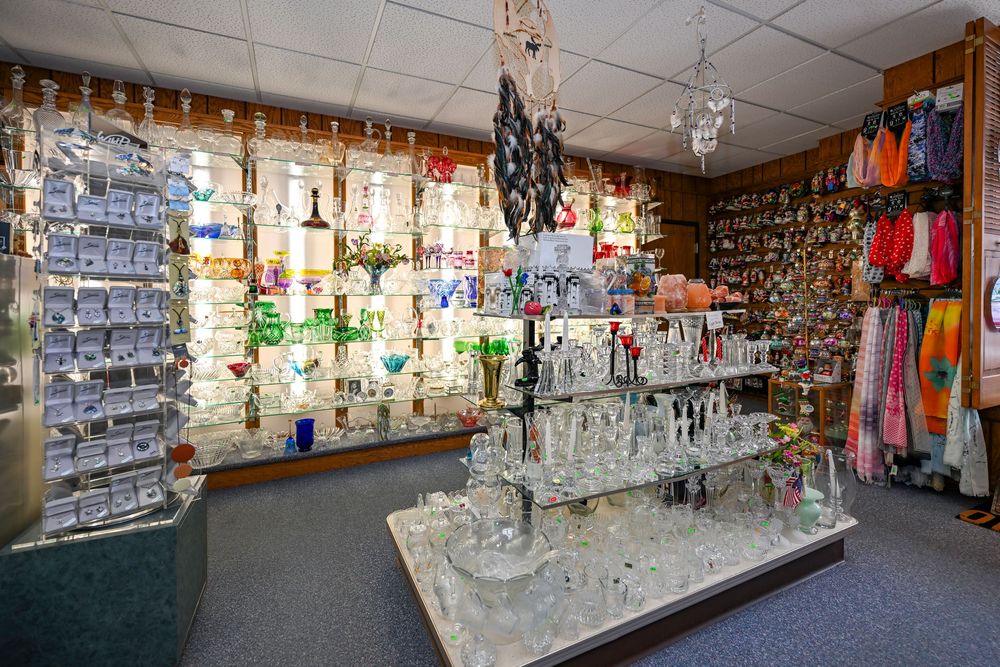 Interior of a glass art gift shop displaying crystal figurines, colorful glassware, and decorative items on shelves and tables.