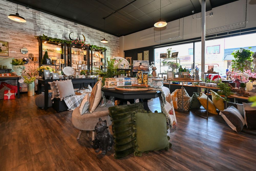 Cozy home decor boutique interior with wood floors, pillows, plants, and eclectic furnishings in a bright retail space.