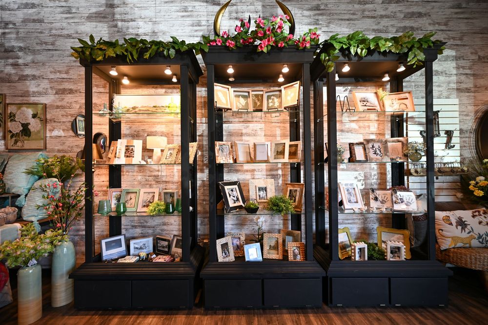 Black display cabinets filled with framed photos and decor in a rustic brick-walled shop adorned with greenery.
