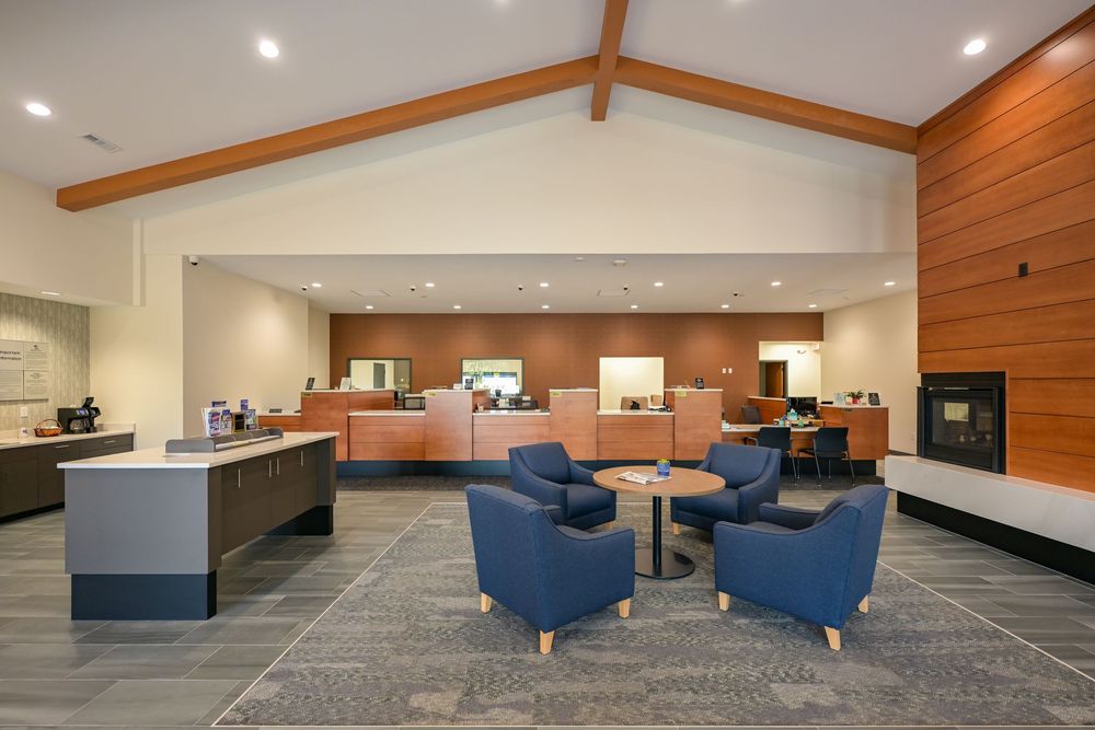 Modern hotel lobby with blue armchairs, wood accents, vaulted ceiling, and a front desk reception area.